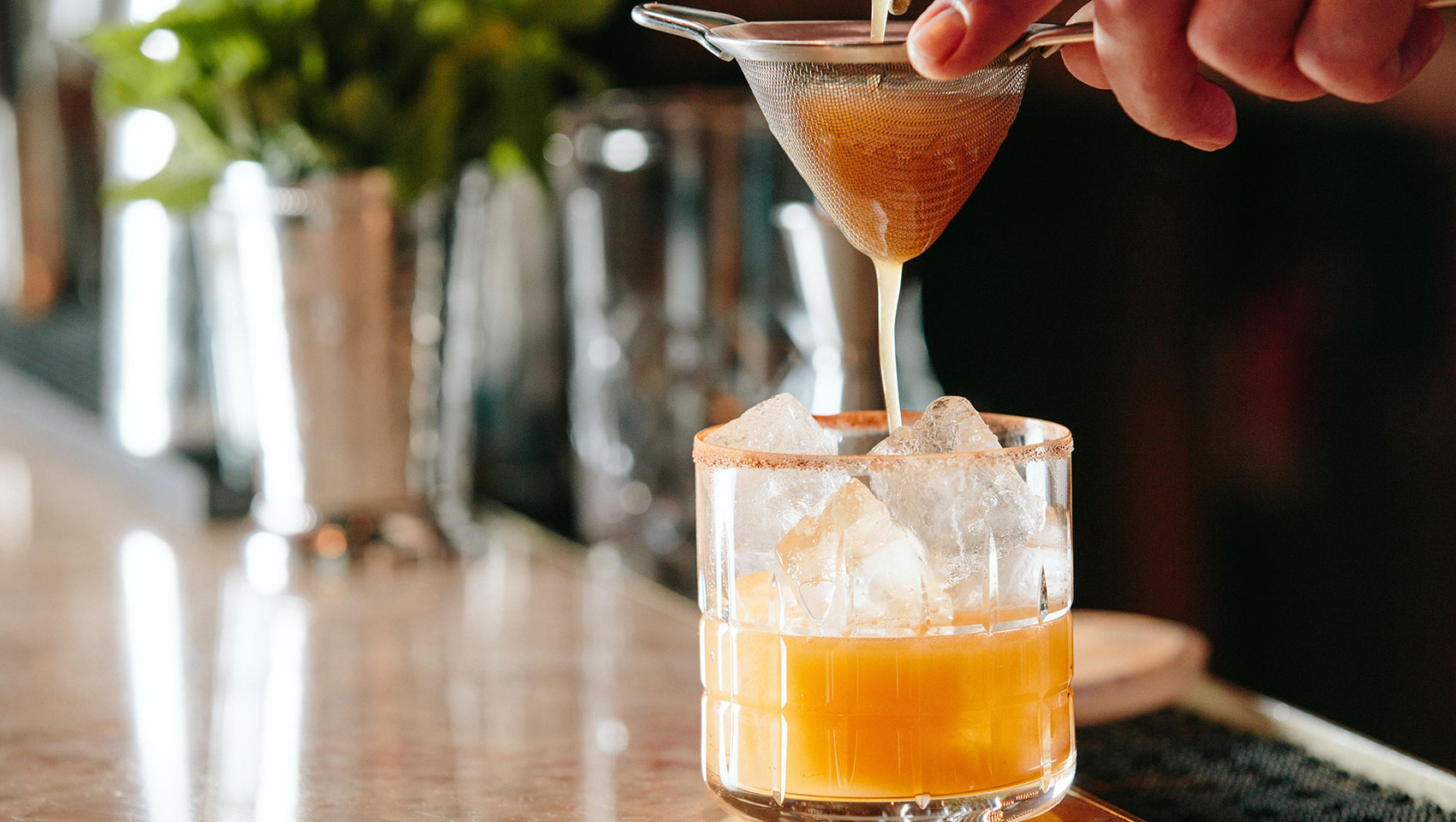 orange craft cocktail being strained and poured