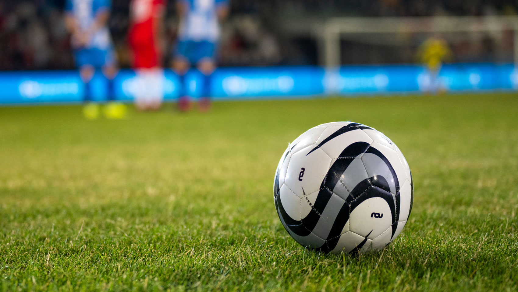 Soccer ball on pitch with players in the background