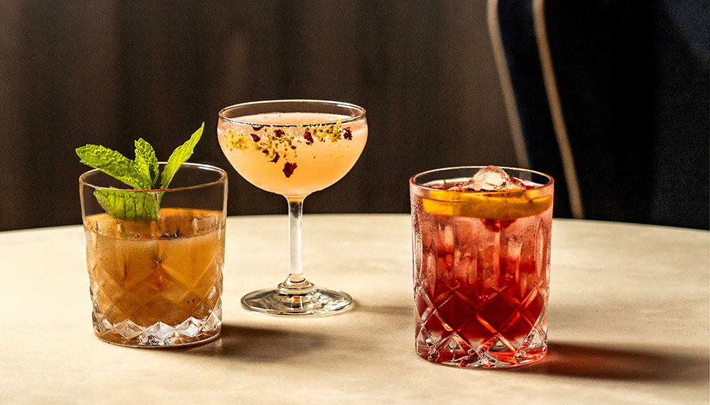Three craft cocktails garnished with mint, citrus, and ice
