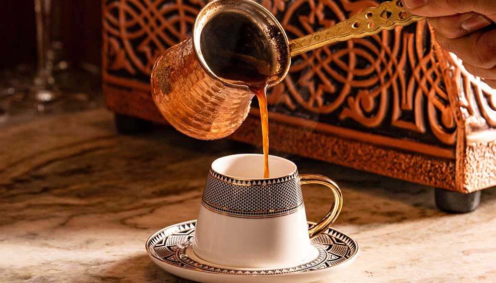 Turkish coffee poured into cup from copper cezve